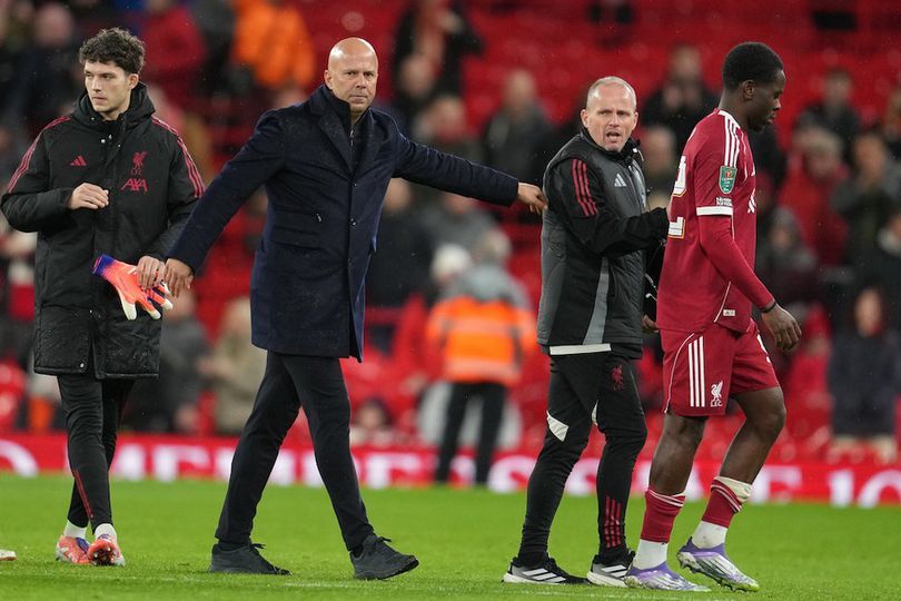 Arne Slot, manajer Liverpool, berjalan di tepi lapangan Anfield dengan mengenakan jaket klub, terlihat fokus mengawasi pertandingan atau latihan.
