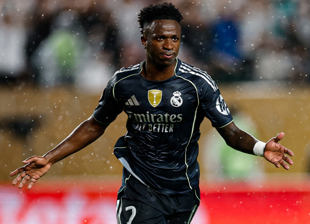 Vinicius Junior mengenakan jersey tandang Real Madrid berwarna hitam dengan ekspresi merayakan gol di lapangan hijau