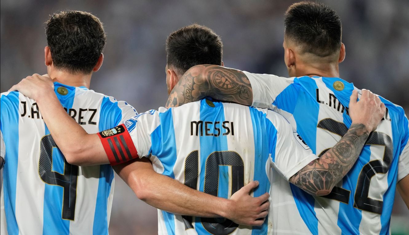 Tampak belakang Lionel Messi mengenakan ban kapten merangkul rekan setimnya di Timnas Argentina saat pertandingan.