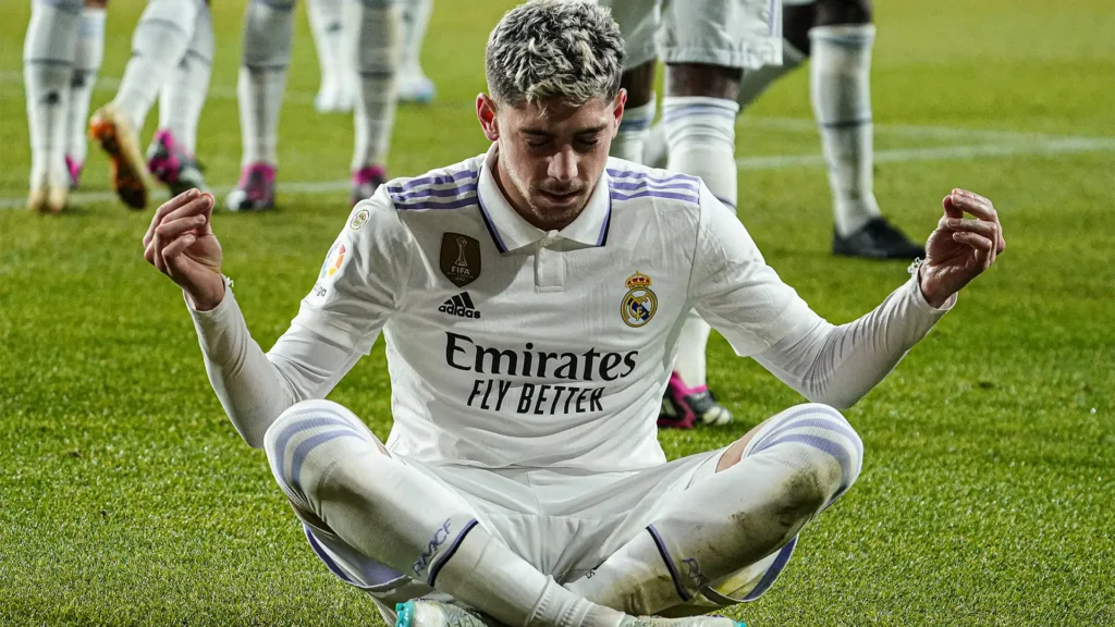 Federico Valverde duduk di lapangan merayakan gol, tangannya menunjuk ke langit.