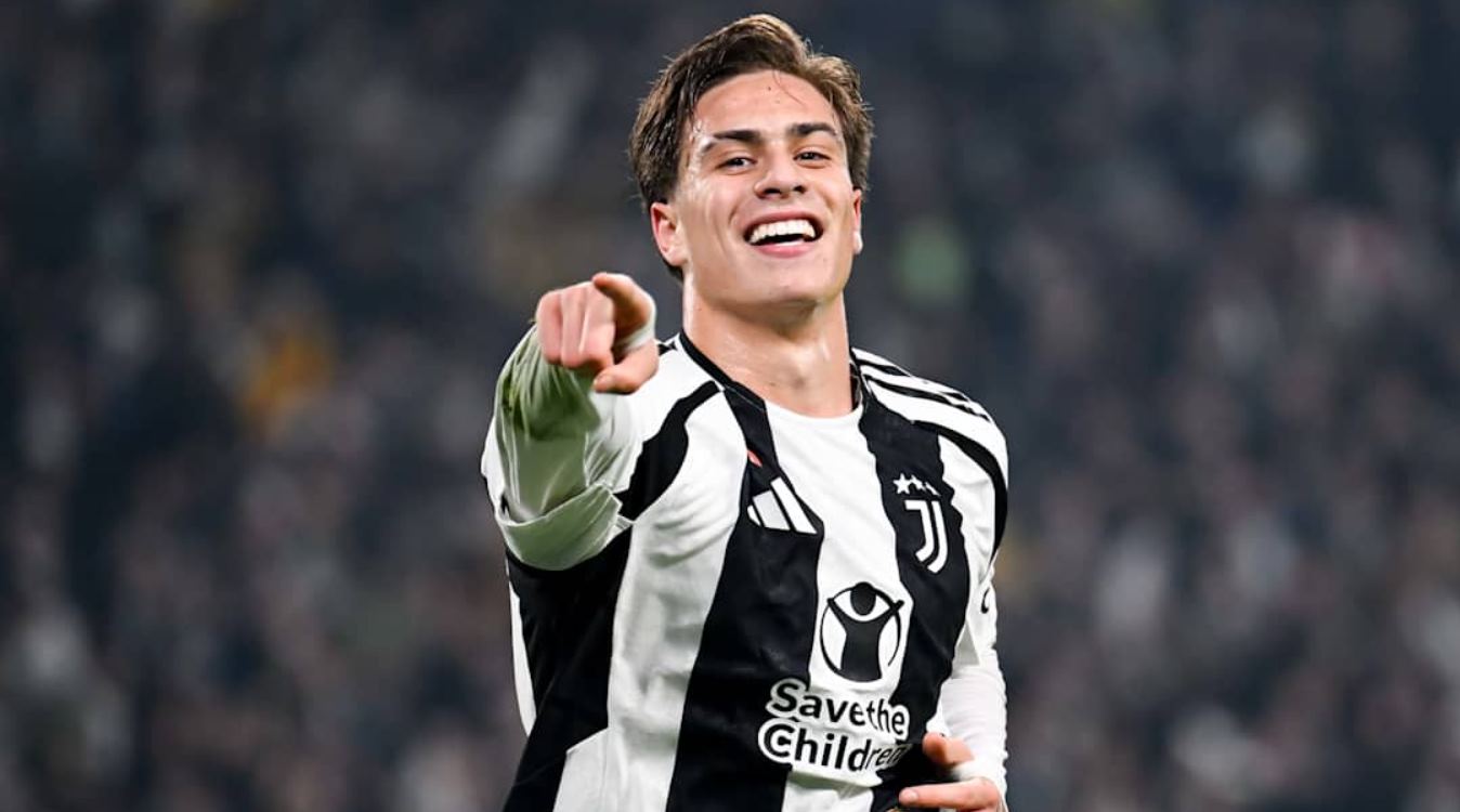 Kenan Yildiz tersenyum dan menunjuk ke arah tribun penonton saat mengenakan jersey Juventus.