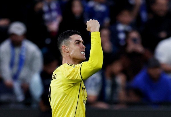 Cristiano Ronaldo mengenakan jersey kuning Al Nassr sedang mengepalkan tangan ke atas merayakan gol di hadapan penonton.