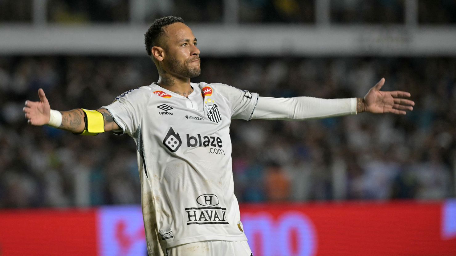 Neymar Jr dengan ban kapten di lengan, merentangkan kedua tangan merayakan performanya bersama Santos FC di hadapan penonton.