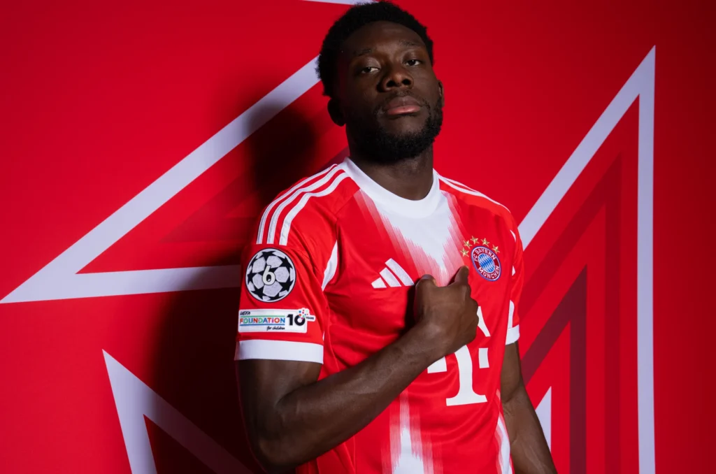 Alphonso Davies menggunakan jersey Bayern Munchen dengan latar belakang merah, target transfer bek kiri Manchester United