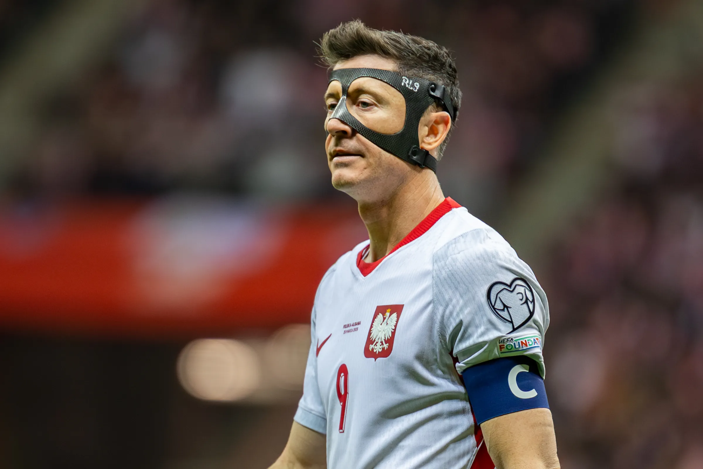 Robert Lewandowski mengenakan jersey timnas Polandia dan masker pelindung wajah, tampak kecewa di lapangan setelah pertandingan