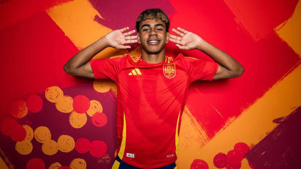 Lamine Yamal mengenakan jersei Timnas Spanyol melakukan selebrasi ikonik dengan tangan di telinga.