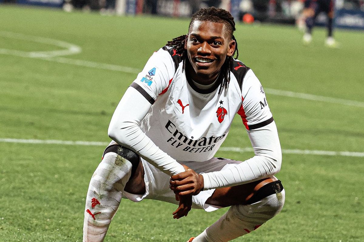 Pemain sayap AC Milan Rafael Leao mengenakan jersi tandang putih, sedang berjongkok di lapangan sepak bola.