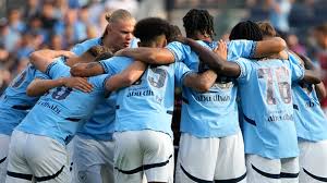 Pemain Manchester City, termasuk Erling Haaland, saling merangkul di lapangan sebagai bentuk solidaritas dan selebrasi tim saat pertandingan.