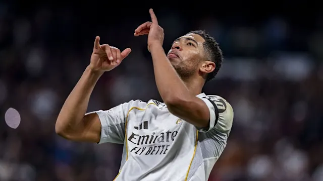 Jude Bellingham mengenakan jersei putih Real Madrid melakukan selebrasi dengan mendongak ke atas sambil menunjuk ke arah langit.