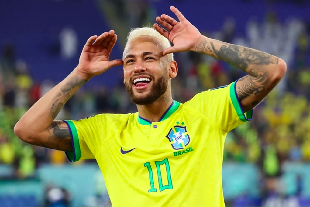 "Neymar Jr. mengenakan jersey timnas Brasil nomor 10 sambil melakukan selebrasi ikonik menjulurkan lidah dan menempelkan telapak tangan terbuka di samping kepalanya di atas lapangan hijau."