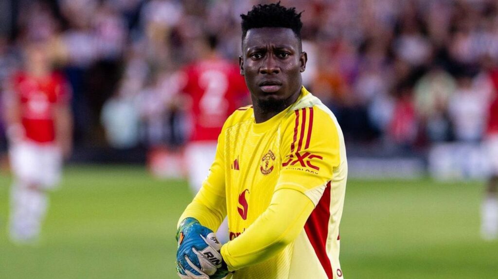 Kiper André Onana mengenakan jersey kuning Manchester United di lapangan hijau.