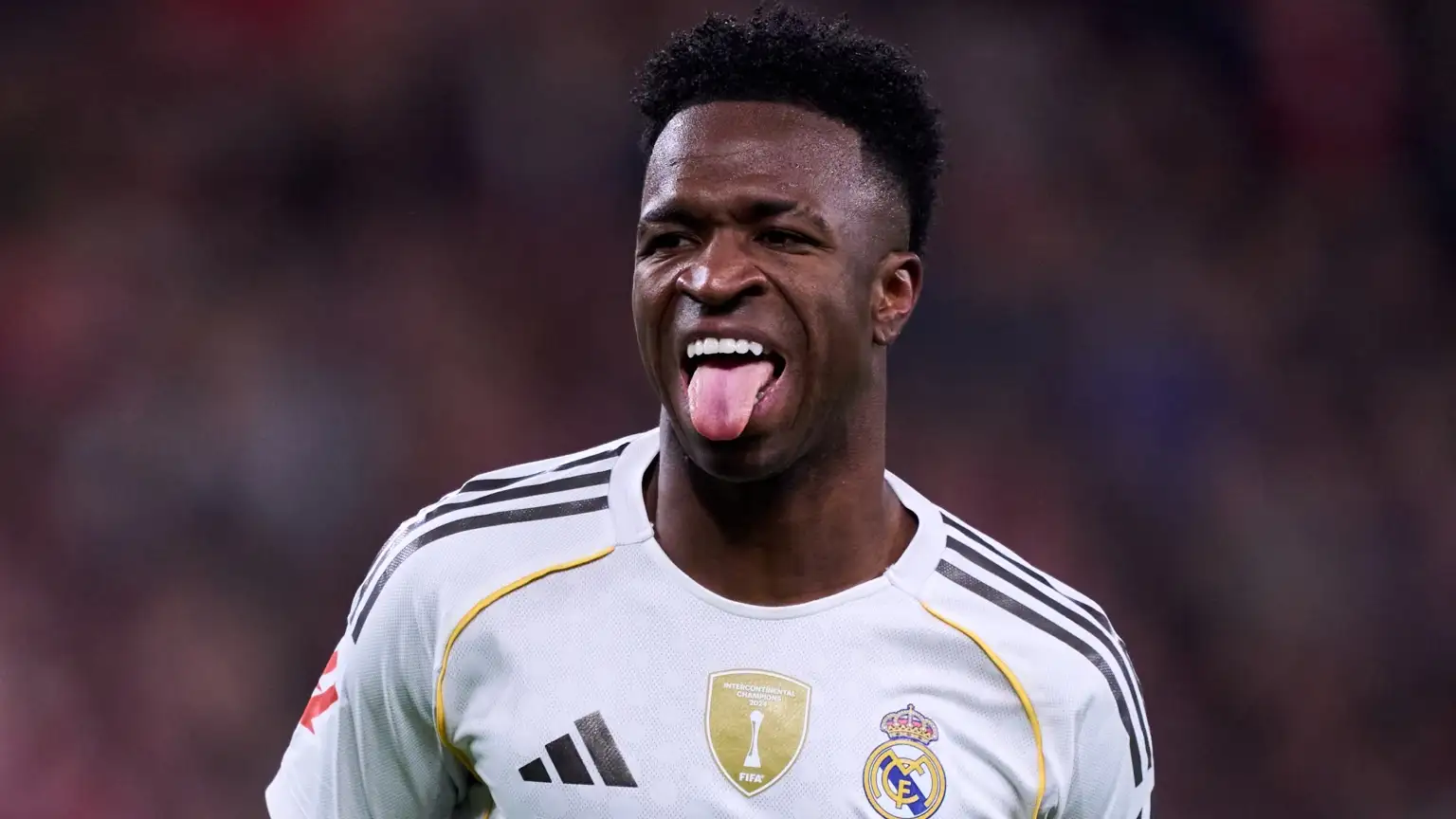 Vinicius Junior menjulurkan lidah saat melakukan selebrasi gol dengan jersey putih Real Madrid.