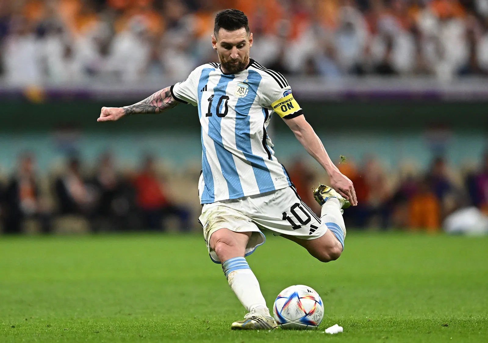 Lionel Messi dengan seragam timnas Argentina sedang menendang bola di lapangan hijau.