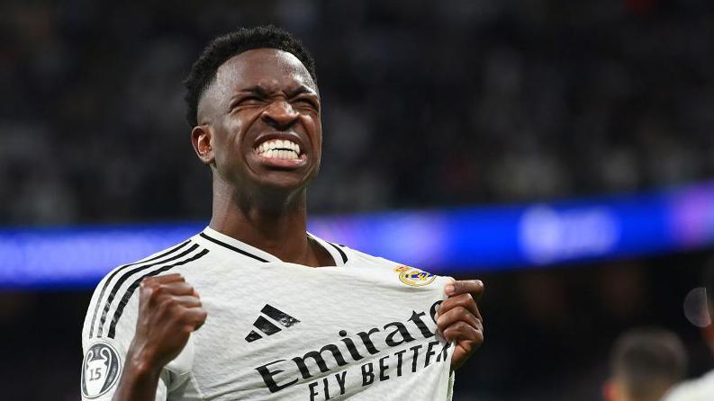 Vinicius Junior merayakan gol dengan emosional sambil memegang lambang klub di jersey Real Madrid.