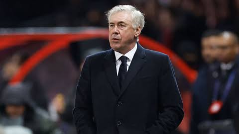 Pelatih Timnas Brasil, Carlo Ancelotti, mengenakan jas hitam saat mendampingi timnya di pinggir lapangan.