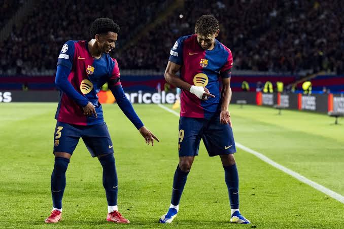 Alejandro Balde dan Jules Kounde menggunakan jersey Barcelona merayakan momen di lapangan hijau.