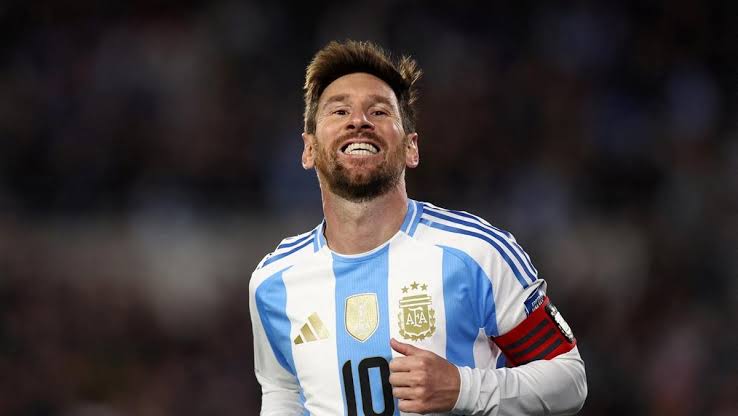 Lionel Messi mengenakan jersi Timnas Argentina tersenyum di lapangan.