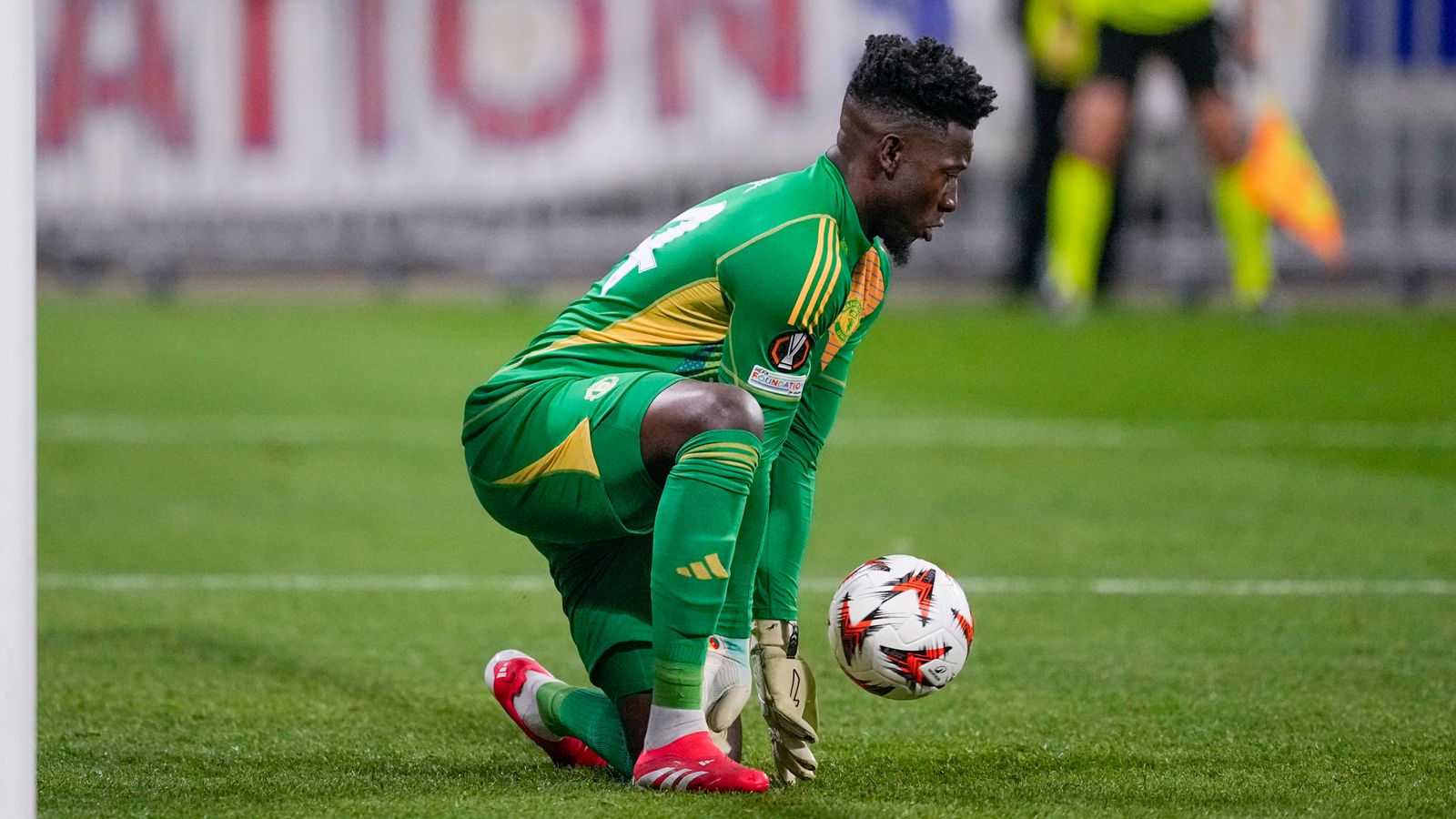 Kiper André Onana berlutut di lapangan hijau dengan seragam kiper berwarna hijau sambil memegang bola.