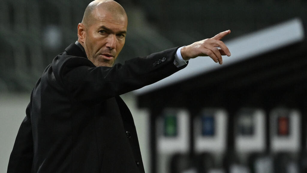 Zinedine Zidane mengenakan pakaian hitam sedang berdiri dan menunjuk ke arah lapangan saat memberi instruksi.