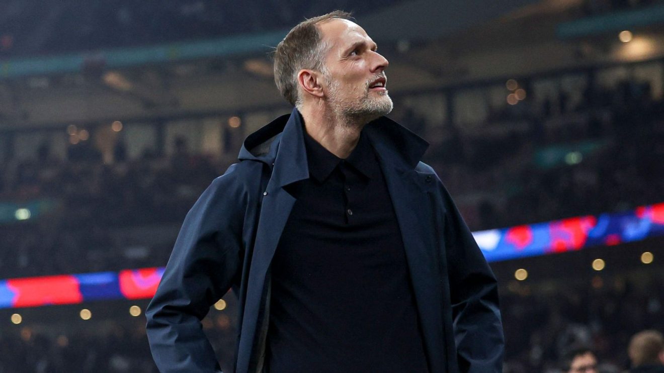 Pelatih Timnas Inggris Thomas Tuchel mengenakan jaket gelap dan mendongak dengan ekspresi lesu di pinggir lapangan stadion.