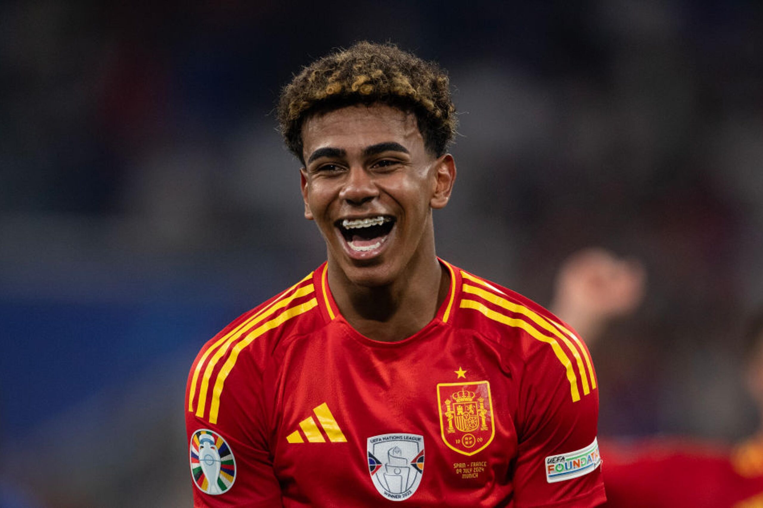 Lamine Yamal mengenakan jersi timnas Spanyol tersenyum lebar di lapangan sepak bola.