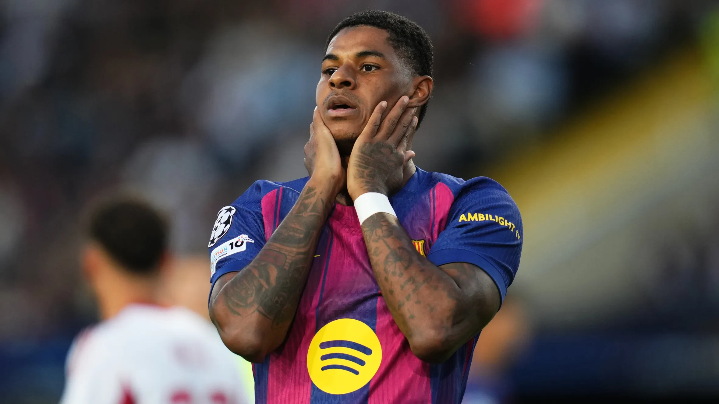 Marcus Rashford mengenakan jersi Barcelona musim 2025/2026 sambil memegang kepalanya di lapangan.