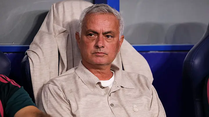 Jose Mourinho sedang duduk di bangku cadangan dengan ekspresi serius.