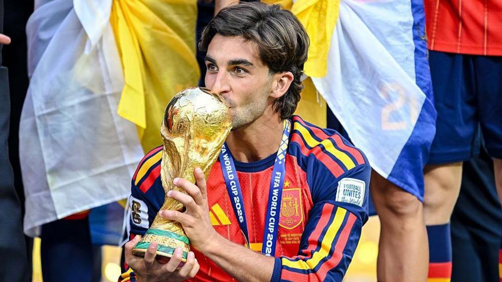 Ferran Torres mencium trofi Piala Dunia saat merayakan kemenangan bersama Timnas Spanyol.