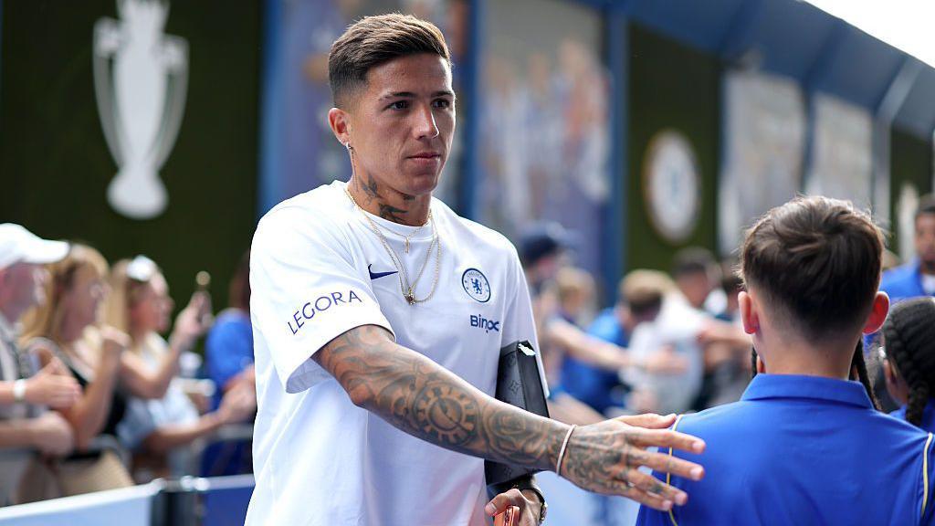 Gelandang Chelsea Enzo Fernandez sedang bersalaman dengan fans di pinggir lapangan.