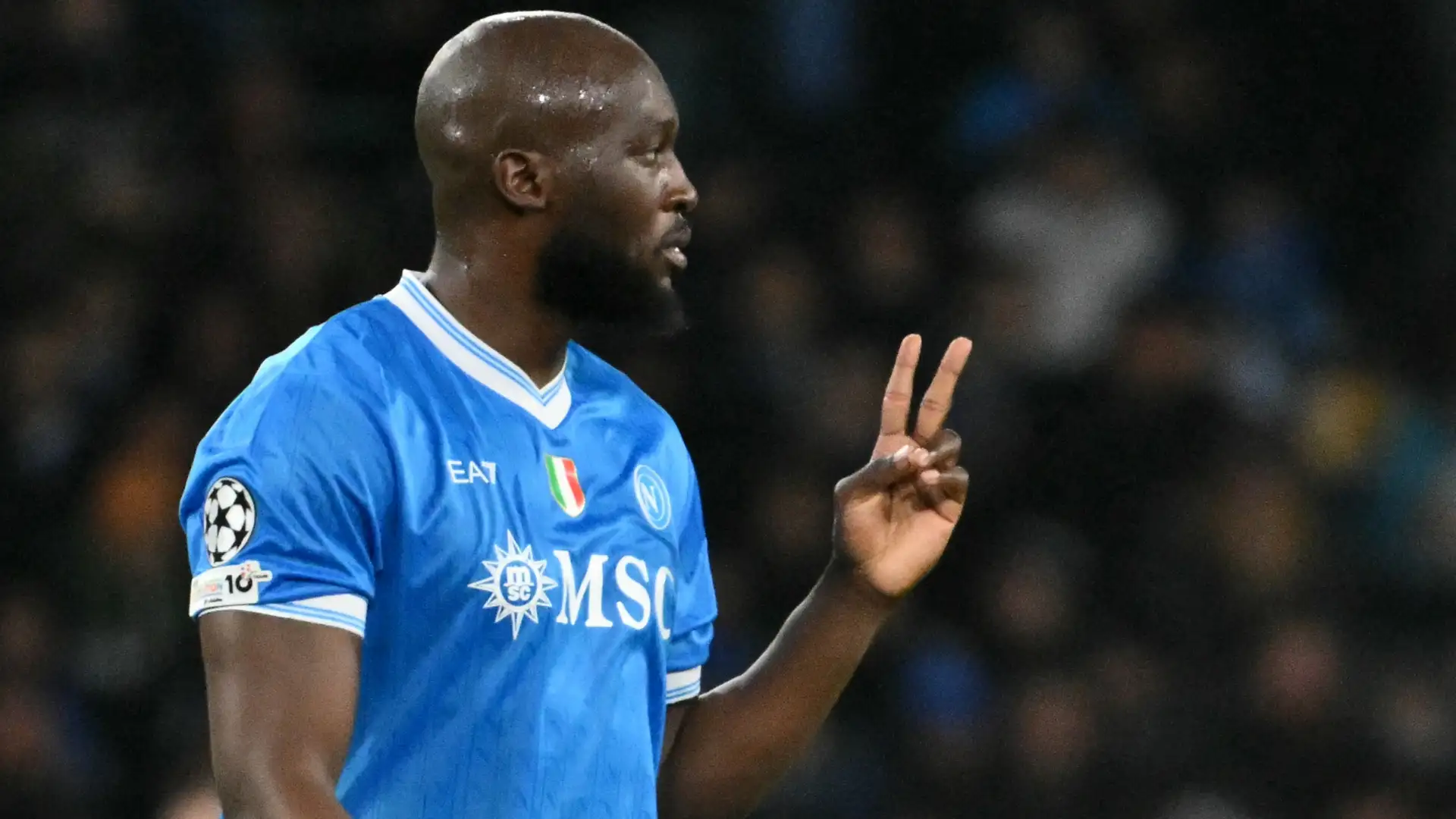 Romelu Lukaku mengenakan jersey biru Napoli sambil memberikan isyarat tangan di lapangan.