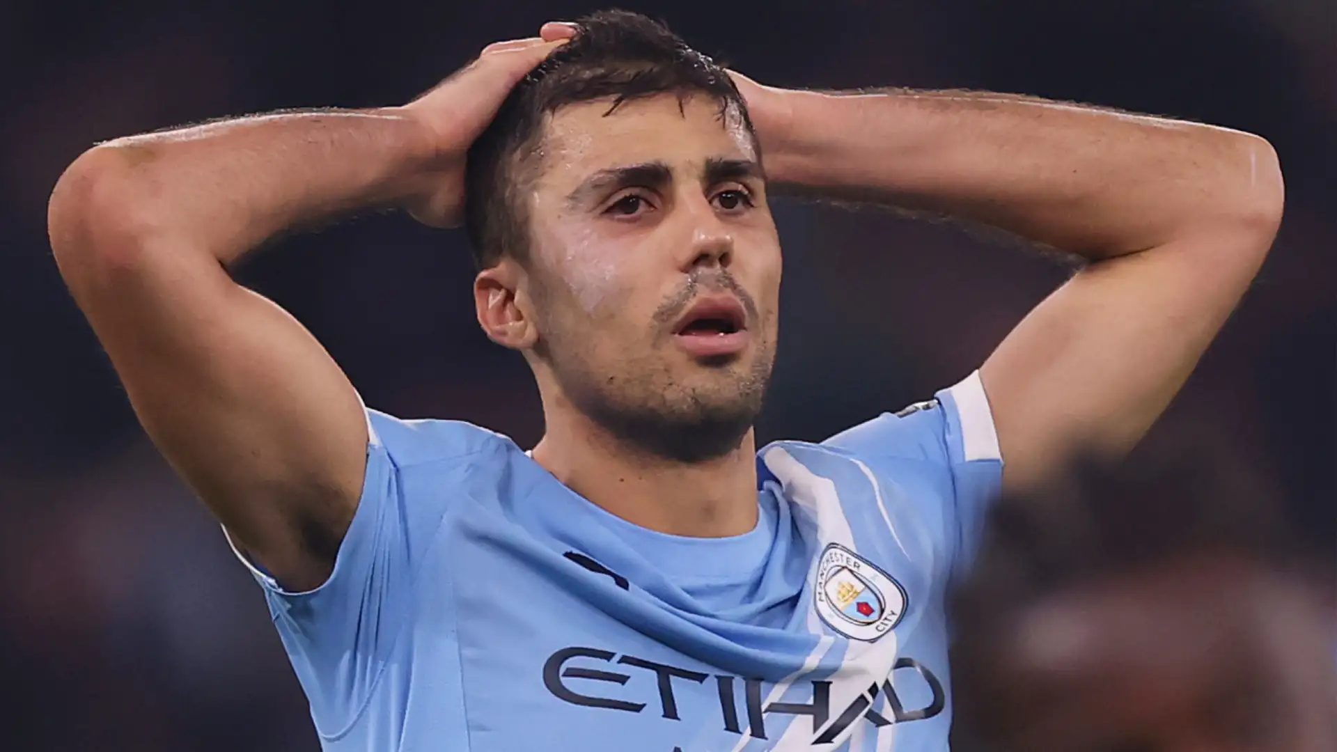 Rodri dengan jersey Manchester City memegang kepala dengan ekspresi kecewa atau khawatir di lapangan.