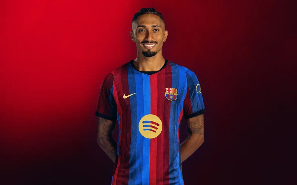Raphinha mengenakan jersey Barcelona dengan latar belakang merah
