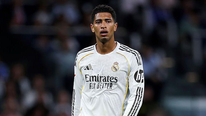 Jude Bellingham berdiri di lapangan menggunakan jersi putih Real Madrid