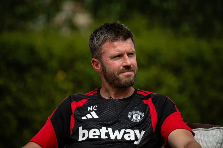 Michael Carrick, pelatih Manchester United, tersenyum dengan latar belakang lapangan hijau